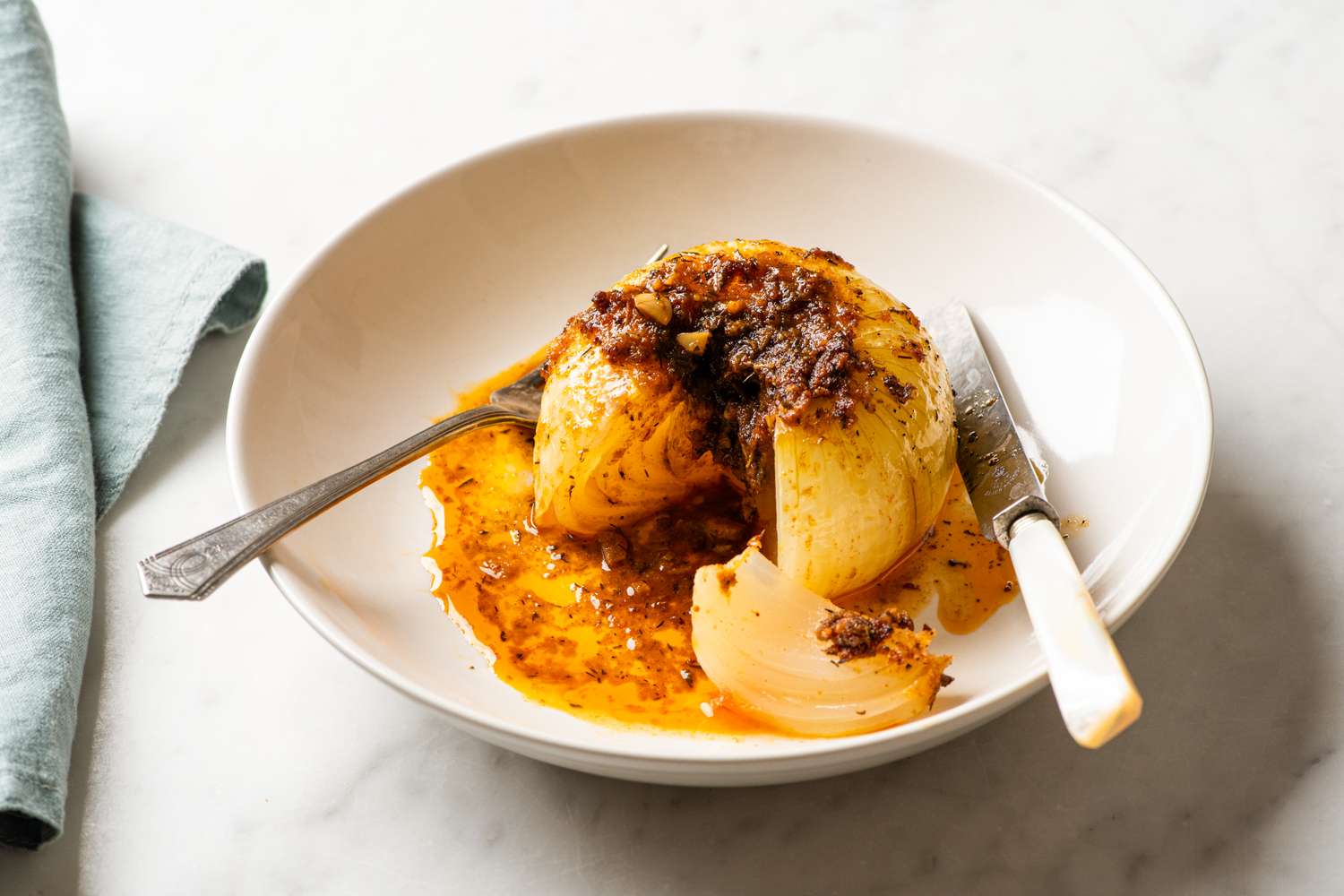 A cooked onion served in a bowl with spices presented with a fork and knife