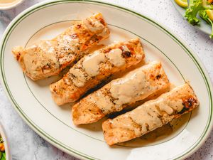 Four salmon fillets garnished with sauce on an oval plate