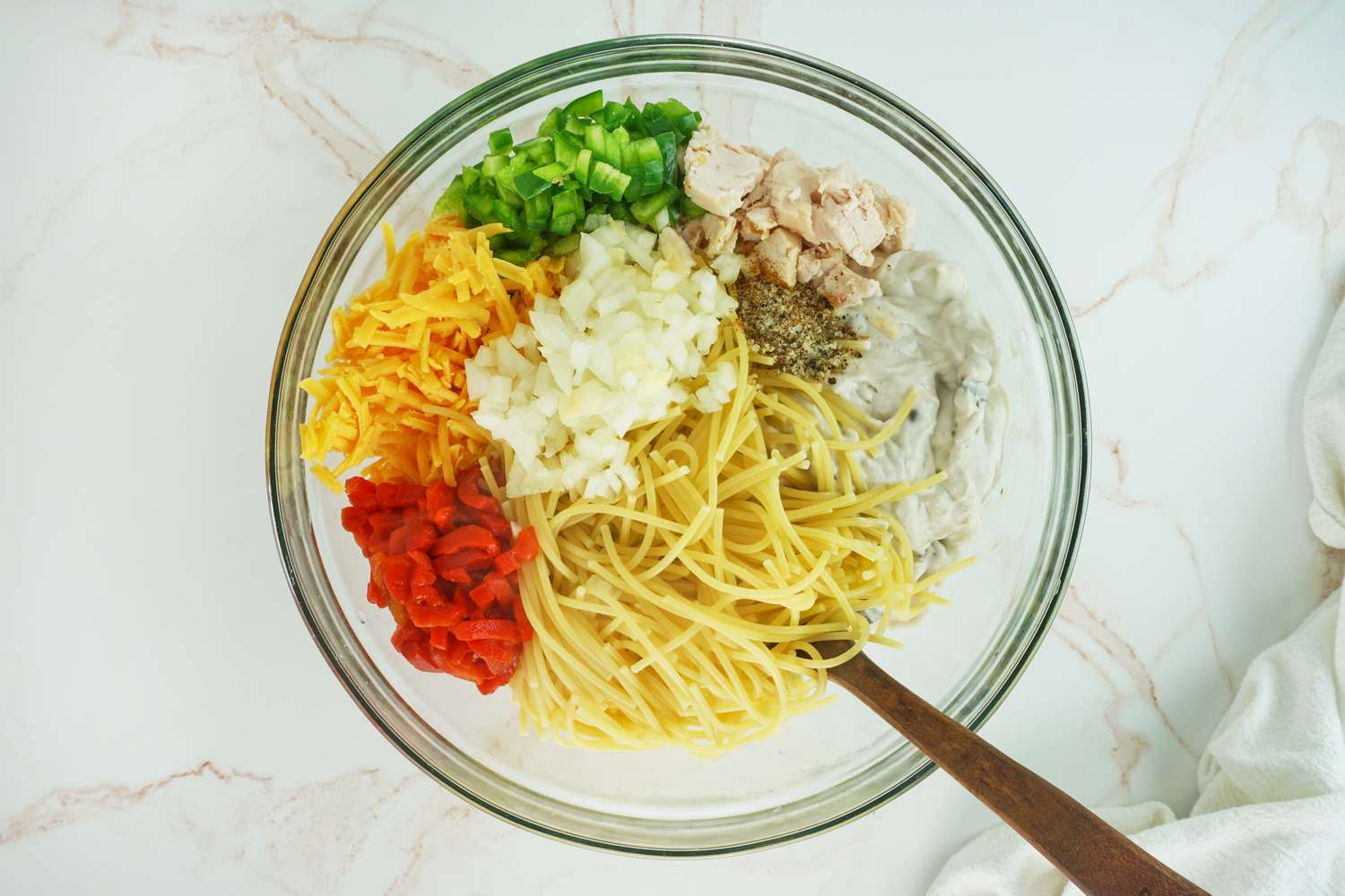 A bowl with uncooked spaghetti shredded cheese diced vegetables cooked chicken and seasonings ingredients for Ree Drummond's Chicken Spaghetti recipe