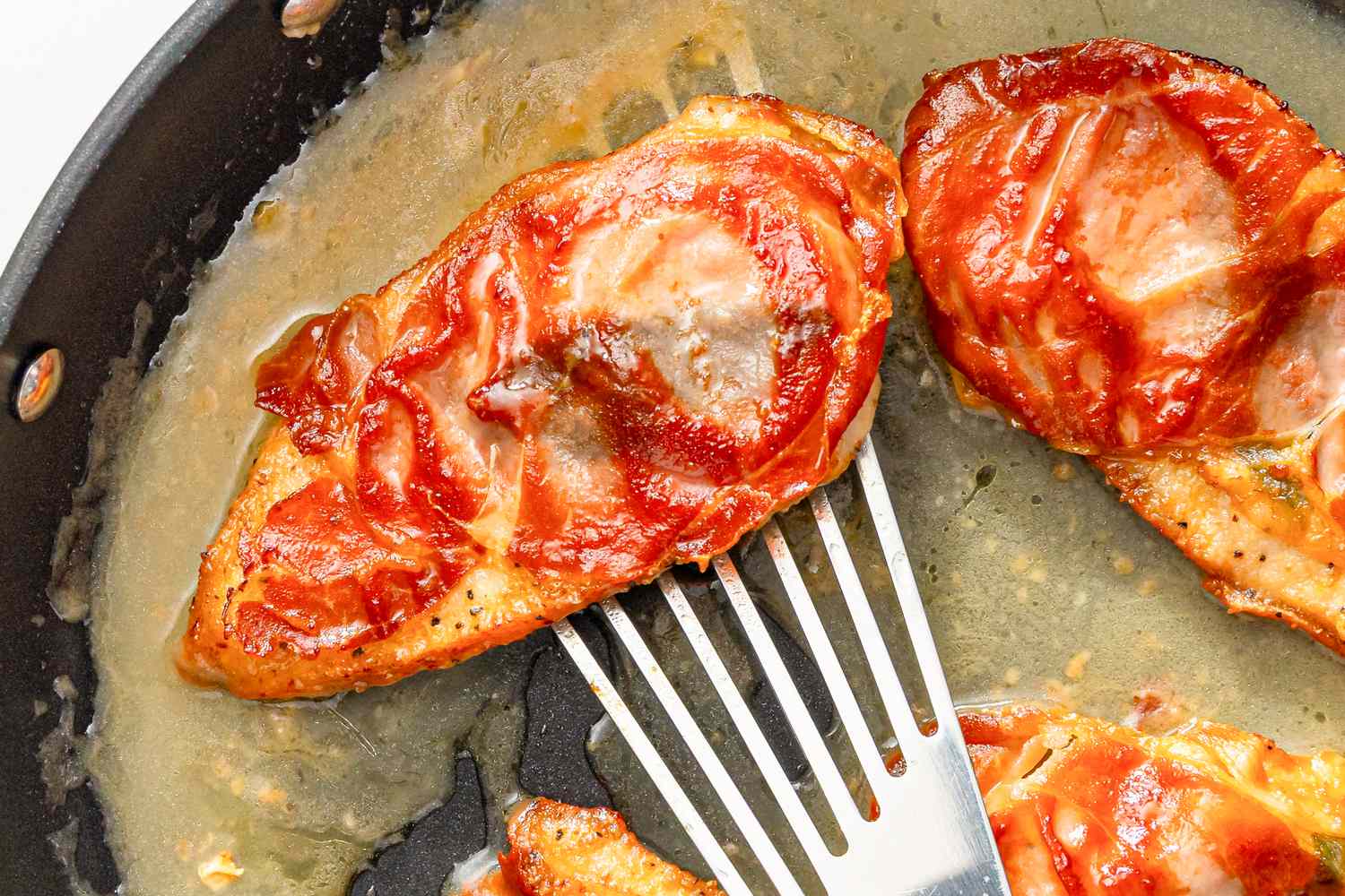 Chicken saltimbocca cooking in a skillet with prosciutto and sauce being handled with a spatula