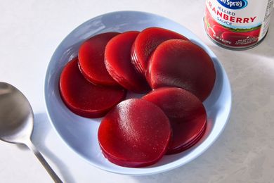 Slices of canned cranberry sauce on a plate next to a spoon and the can