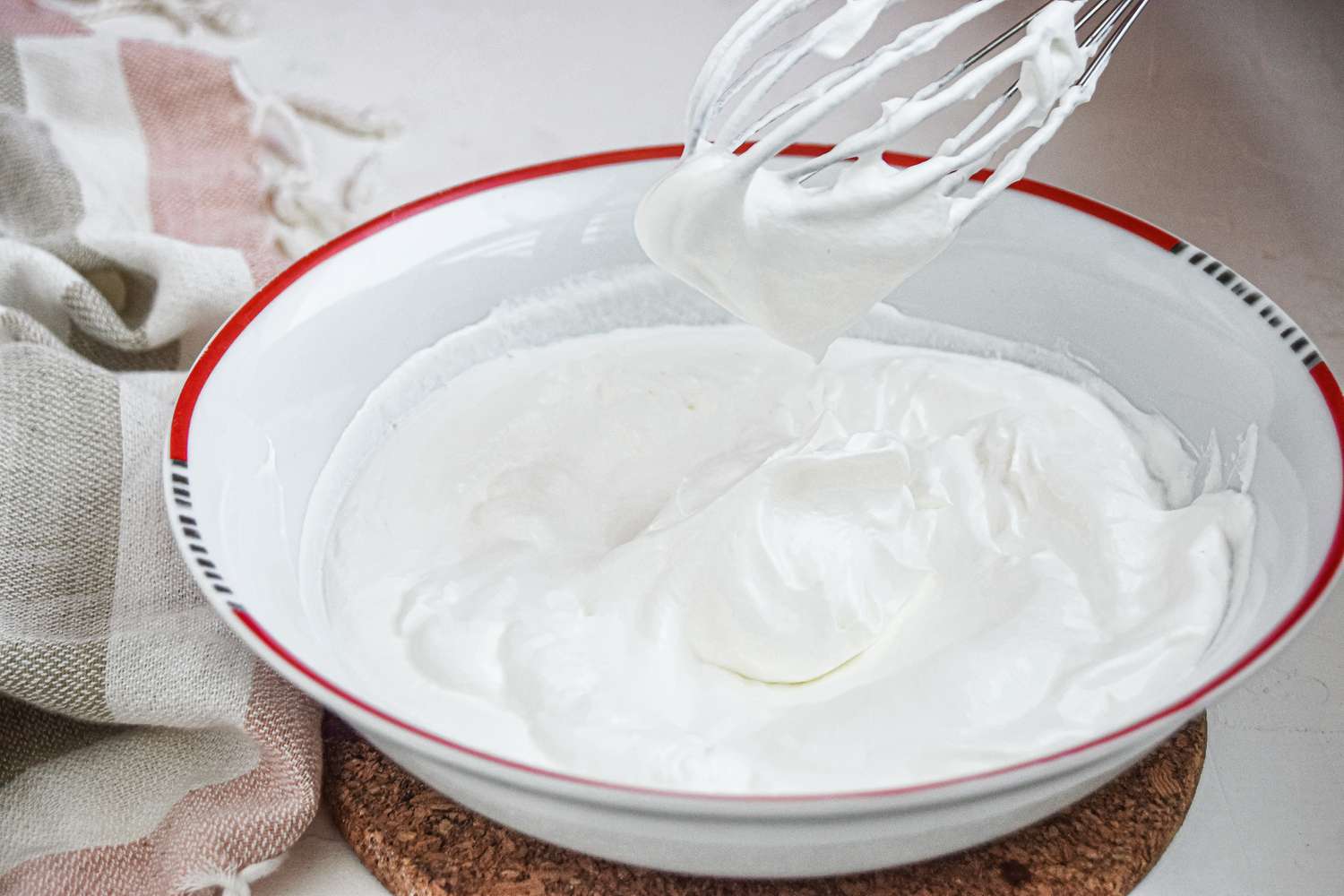 Whisking whipped cream in a white bowl for a custard dessert.