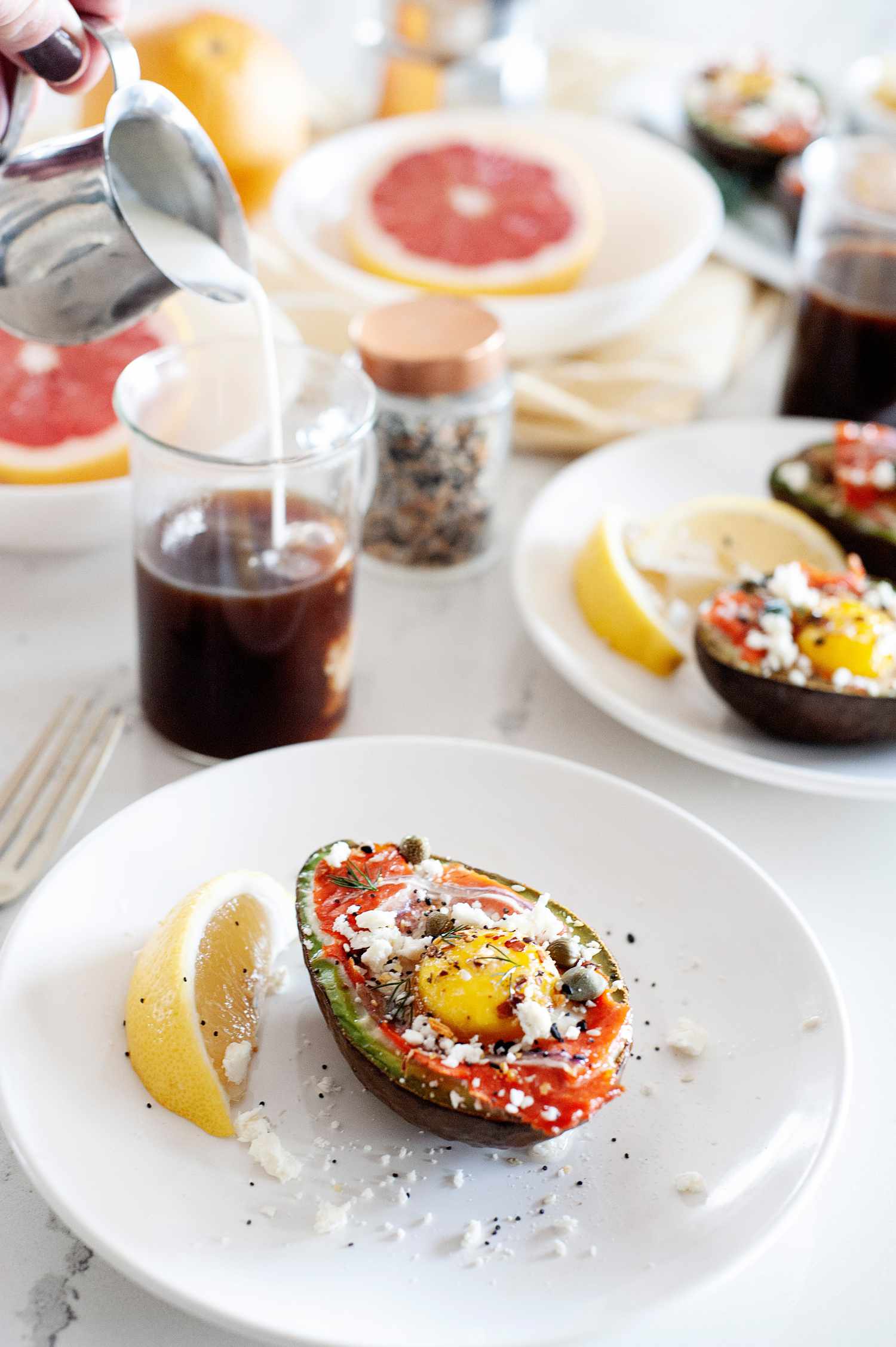 Baked eggs in an avocado on a plate with a lemon. Sliced grapefruit and drinks are behind it.