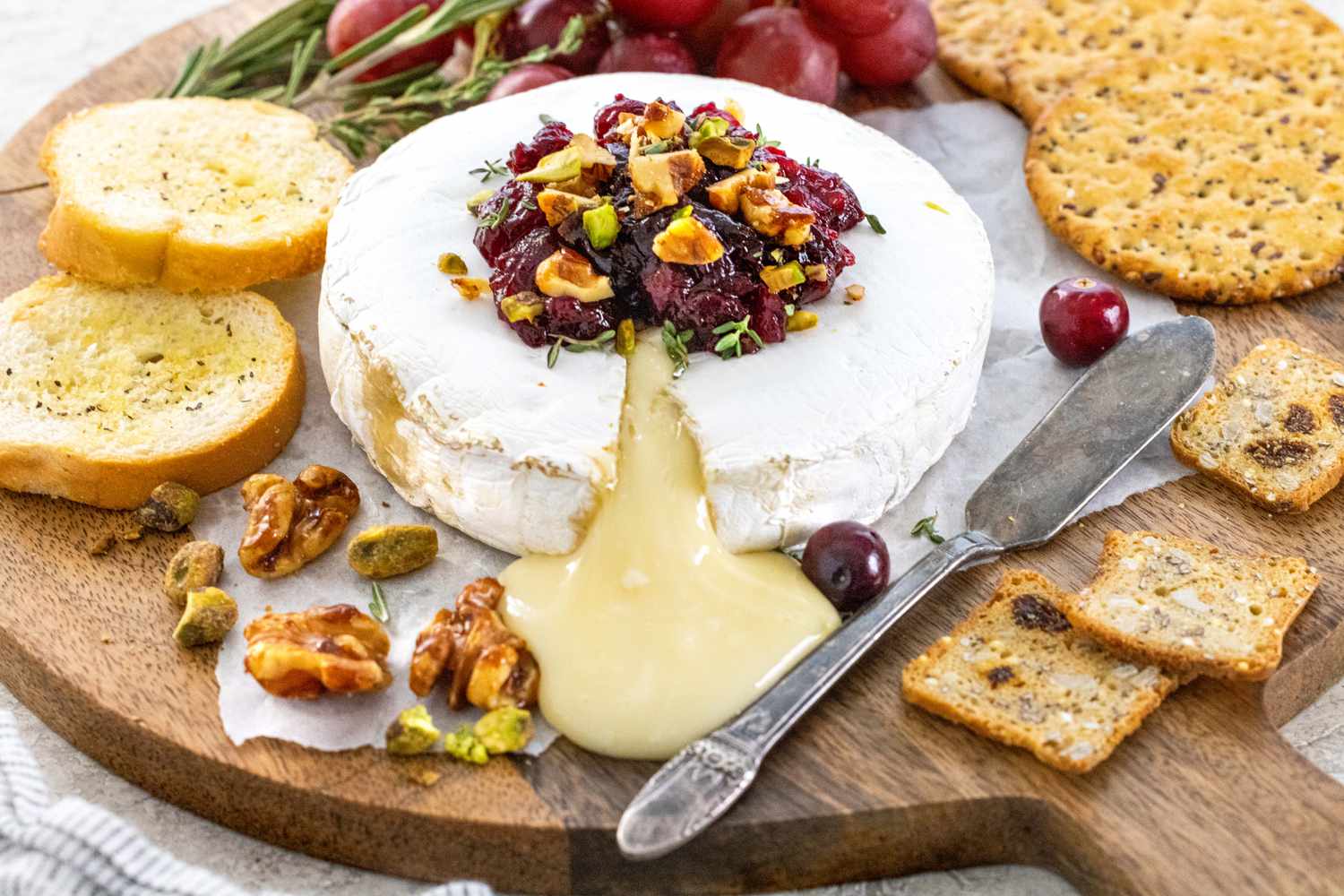 Baked brie with cranberry sauce and candied walnuts on a serving tay with crackers and fruit set around it.