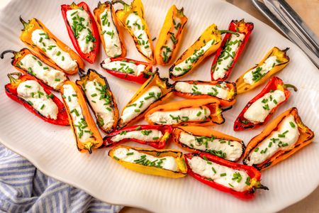 A serving platter of grilled mini peppers stuffed with feta cheese and garnished with chopped herbs