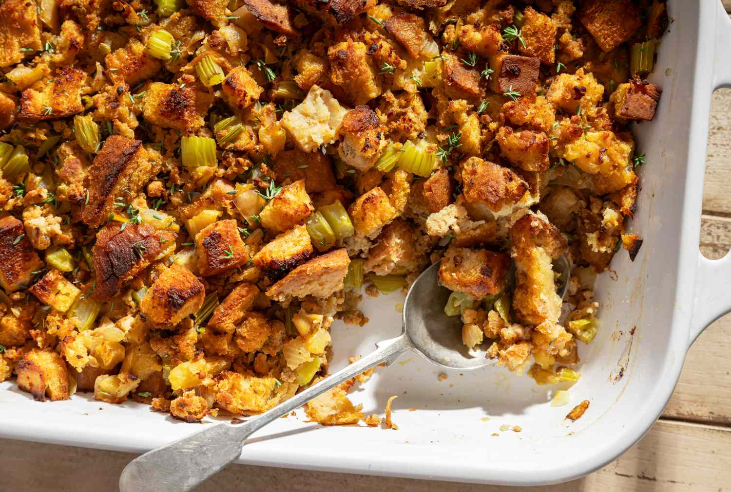A dish of Thanksgiving apple sausage stuffing with a serving spoon placed inside