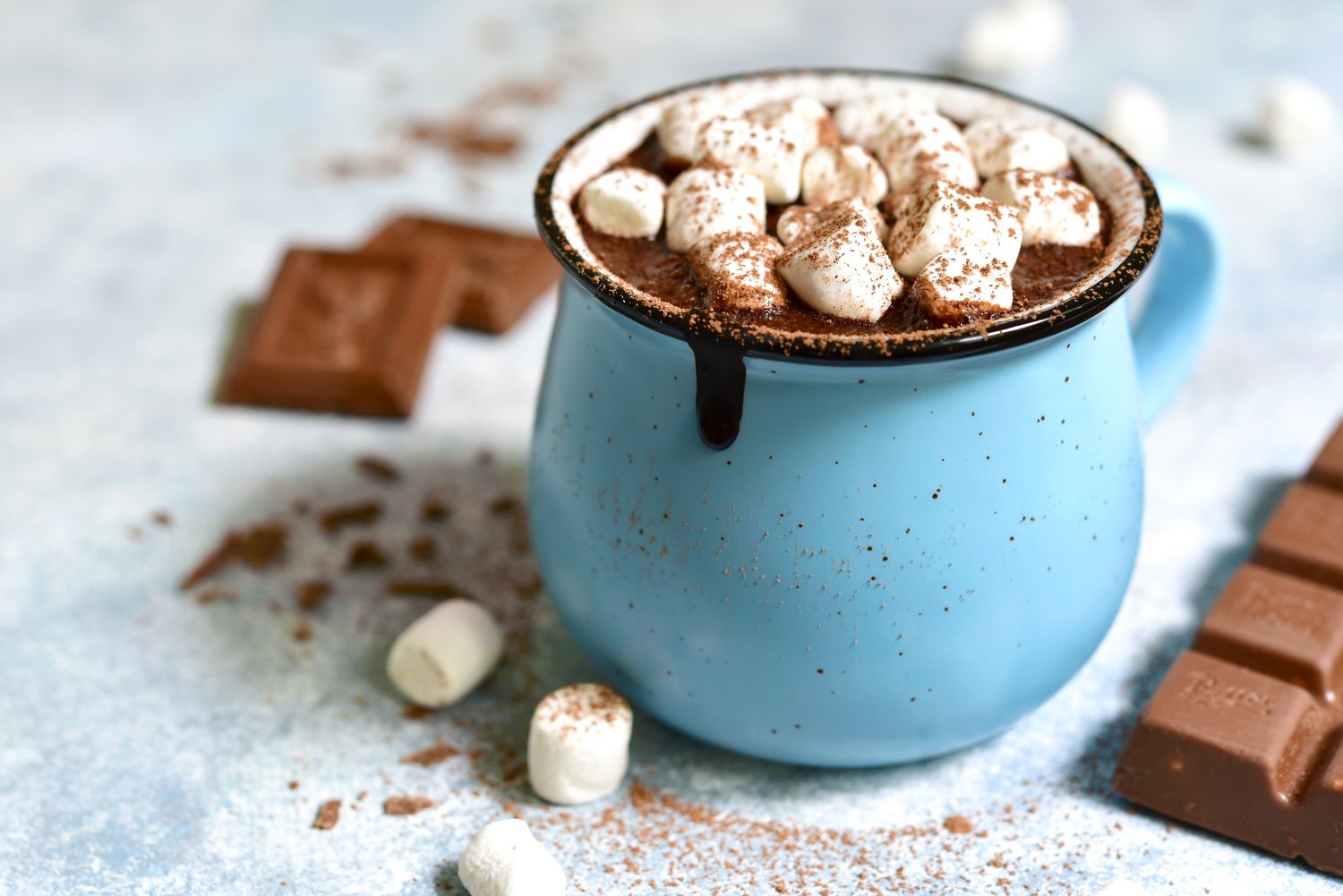 A cup of hot chocolate topped with marshmallows with chocolate bars and cocoa powder nearby