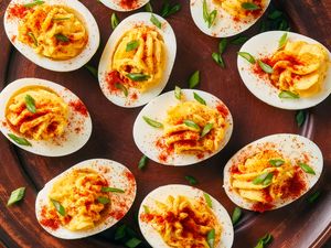 Deviled eggs garnished with paprika and green herbs arranged on a platter