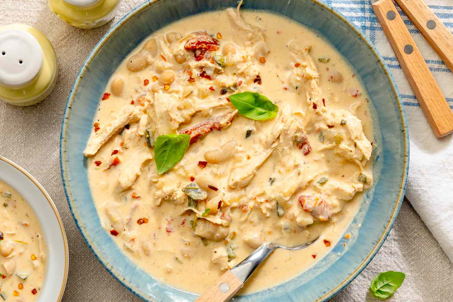 A bowl of creamy chicken chili garnished with herbs and spices with a spoon resting inside