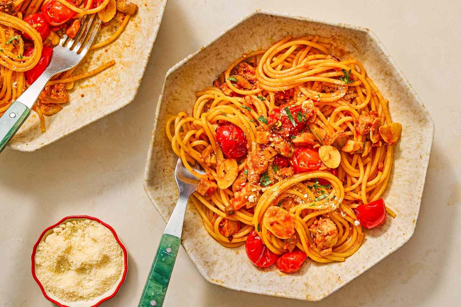 A bowl of spaghetti with cherry tomatoes and herbs next to grated cheese in a small bowl