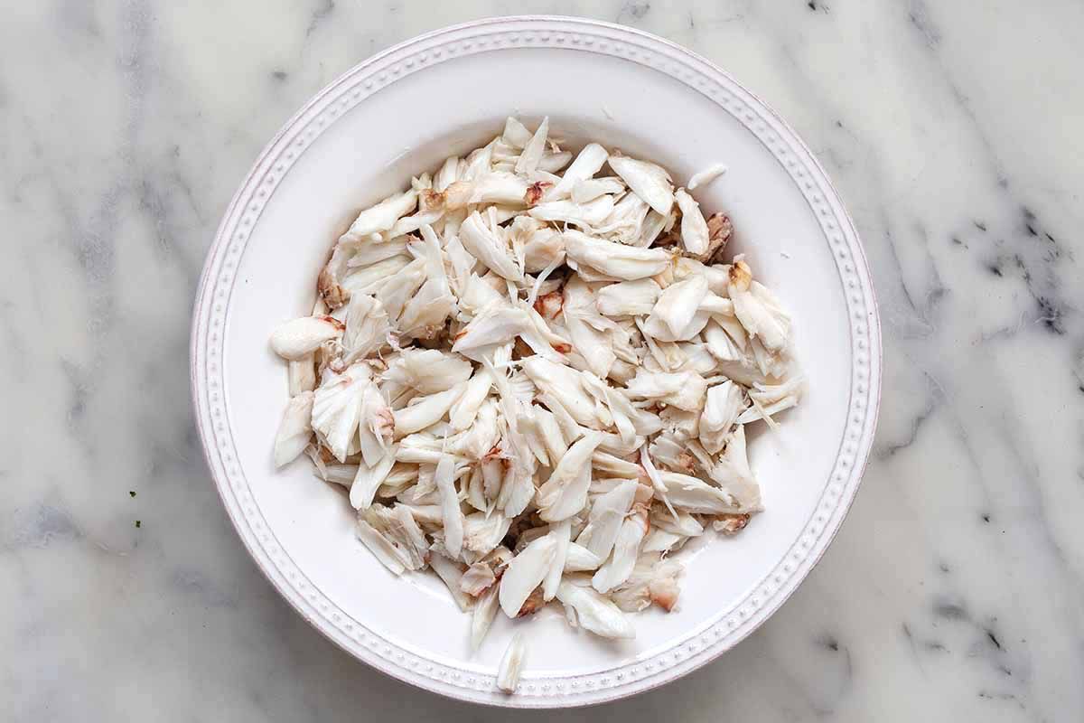 Lump crab meat broken up into smaller pieces on a white plate.