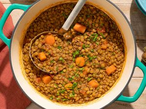 A pot of spiced lentils with carrots garnished with greens and a serving spoon inside