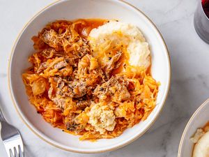 Braised pork roast served over sauerkraut with a side of mashed potatoes in a bowl