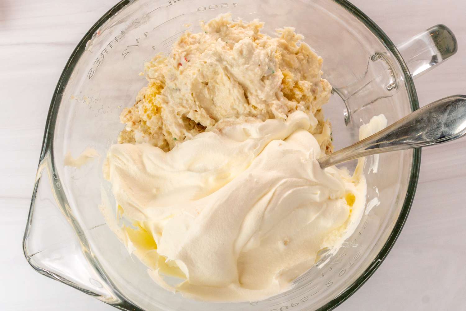 Mixing bowl containing cream and crumbly mixture with a spoon showcasing dish preparation