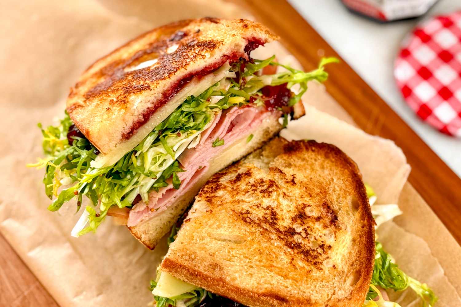 Slices of a sandwich with ham cheese lettuce and jam on toasted bread arranged on parchment paper