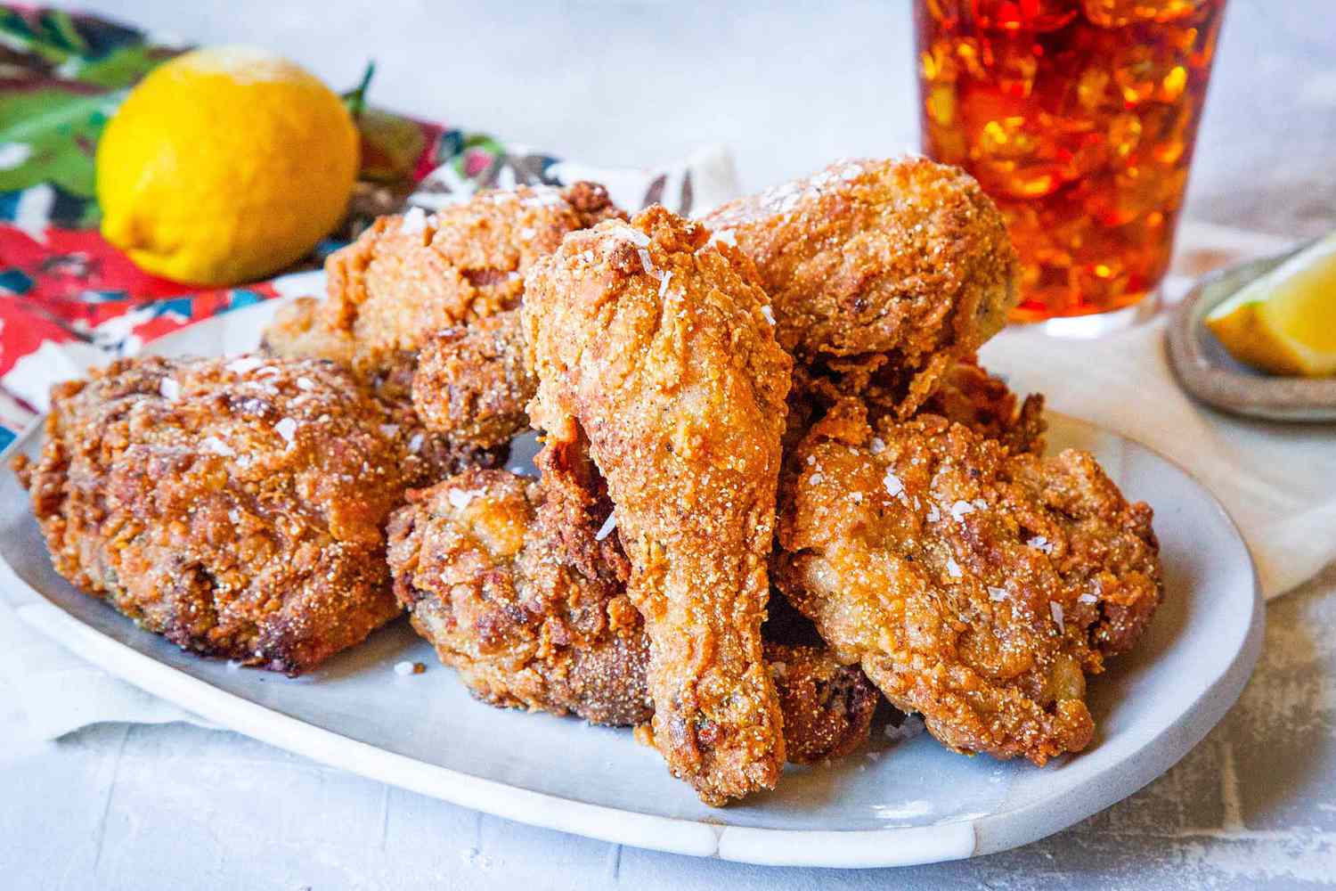 Sweet Tea Fried Chicken on a Platter, and in the Surroundings, a Glass of Ice Tea, a Lemon Wedge on a Small Saucer, and a Lemon on a Colorful Kitchen Towel