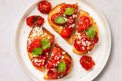 Blistered tomato toast slices garnished with herbs and cheese on a white plate