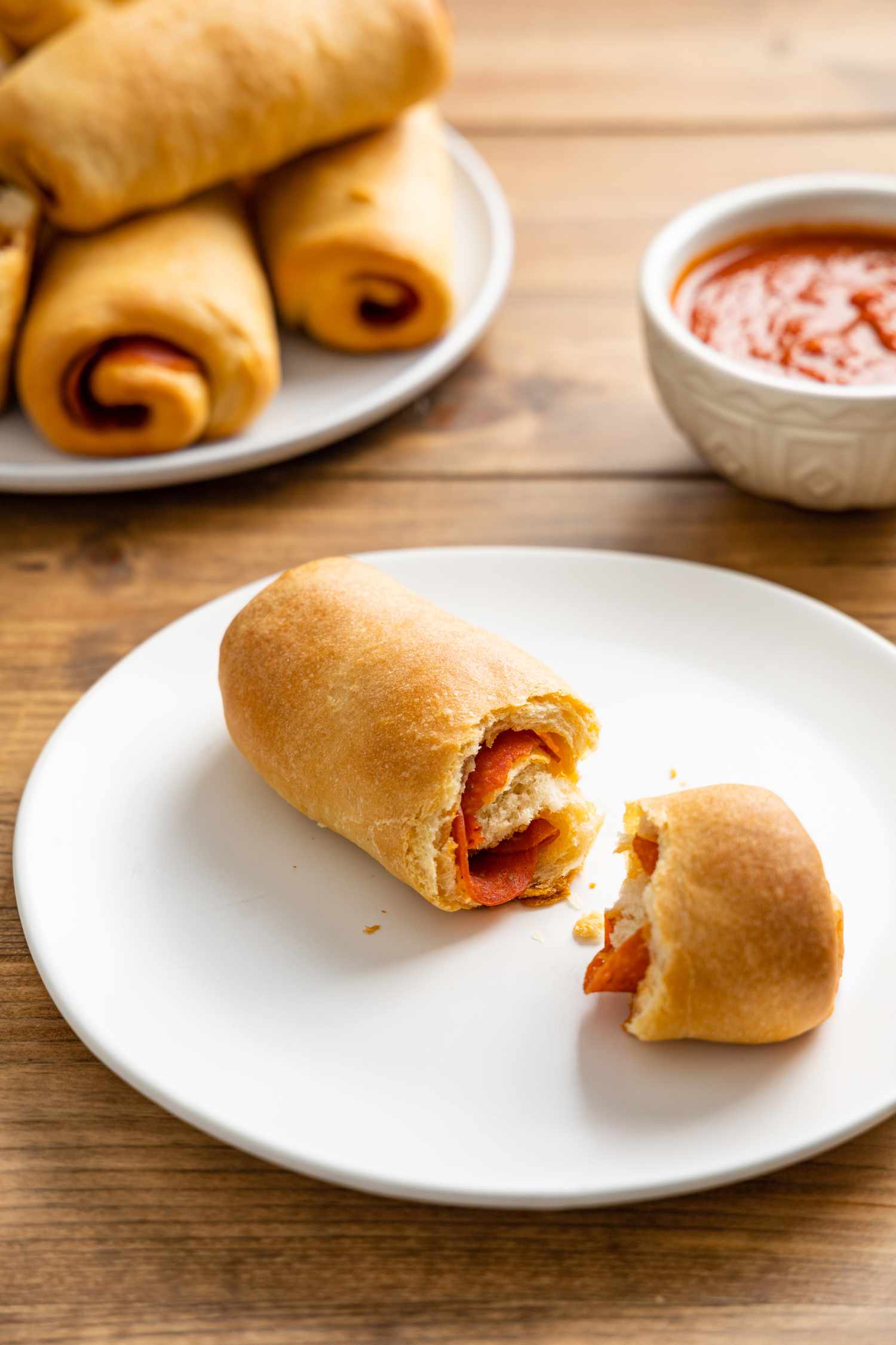 Pepperoni Roll with a Piece Broken on a Plate with a Bowl of Marinara