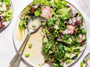 Salad with mixed greens, radish slices, edamame, and a creamy yogurt-based dressing served on a plate with a spoon