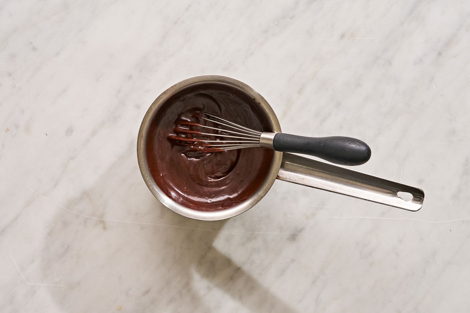 Overhead view of a small saucepan and whisk after melting the butter and adding cocoa powder, milk, vanilla, and salt for Mississippi Mud Cake recipe