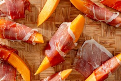 Prosciutto wrapped around melon wedges on a wooden board