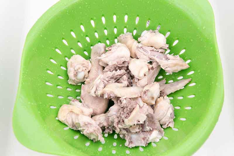 A colander holds shredded chicken for easy chicken noodle soup.