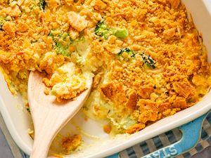 Casserole dish with chicken divan topped with crushed crackers a wooden spoon serving a portion