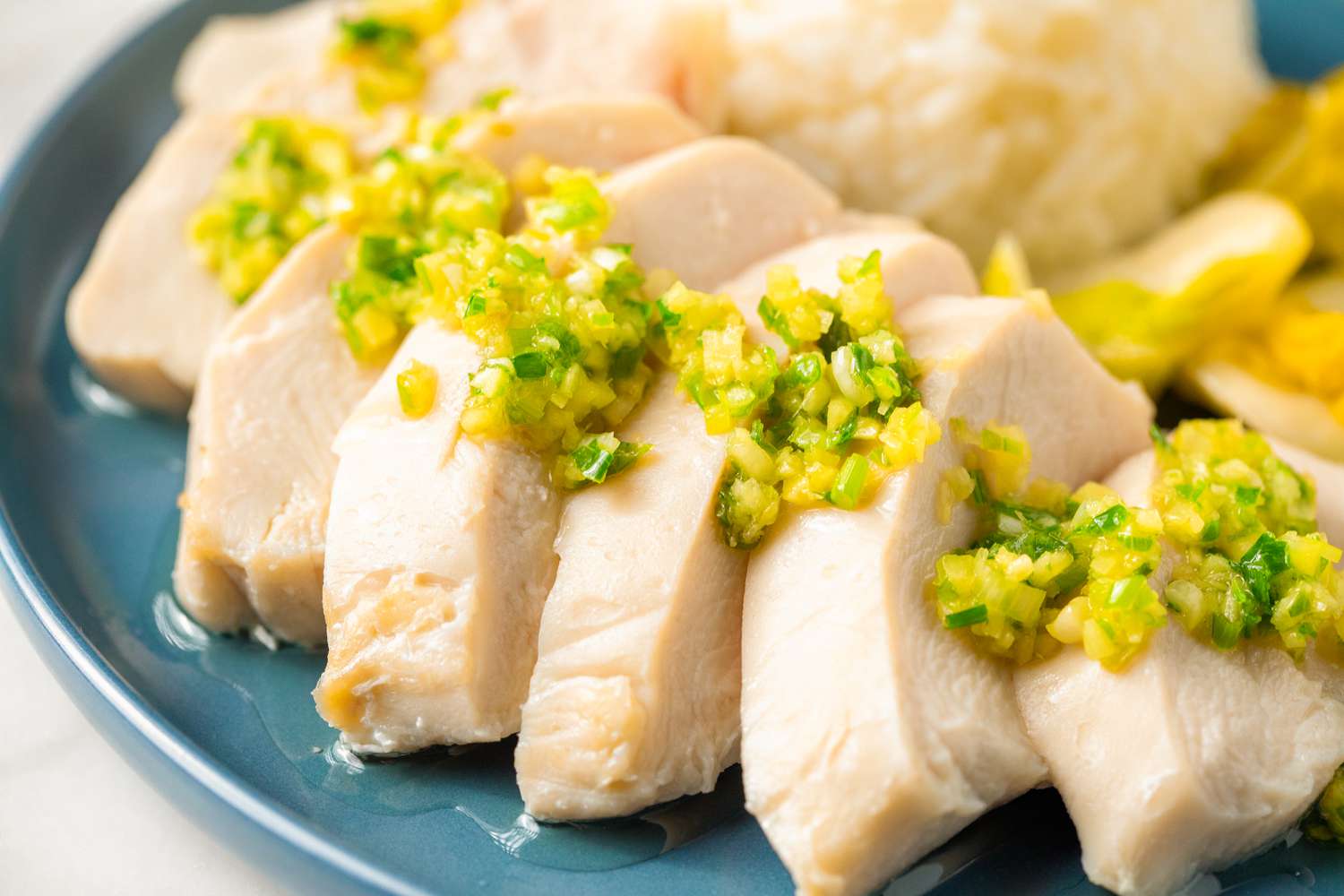 Sliced cooked chicken with a topping of chopped scallions, served on a plate
