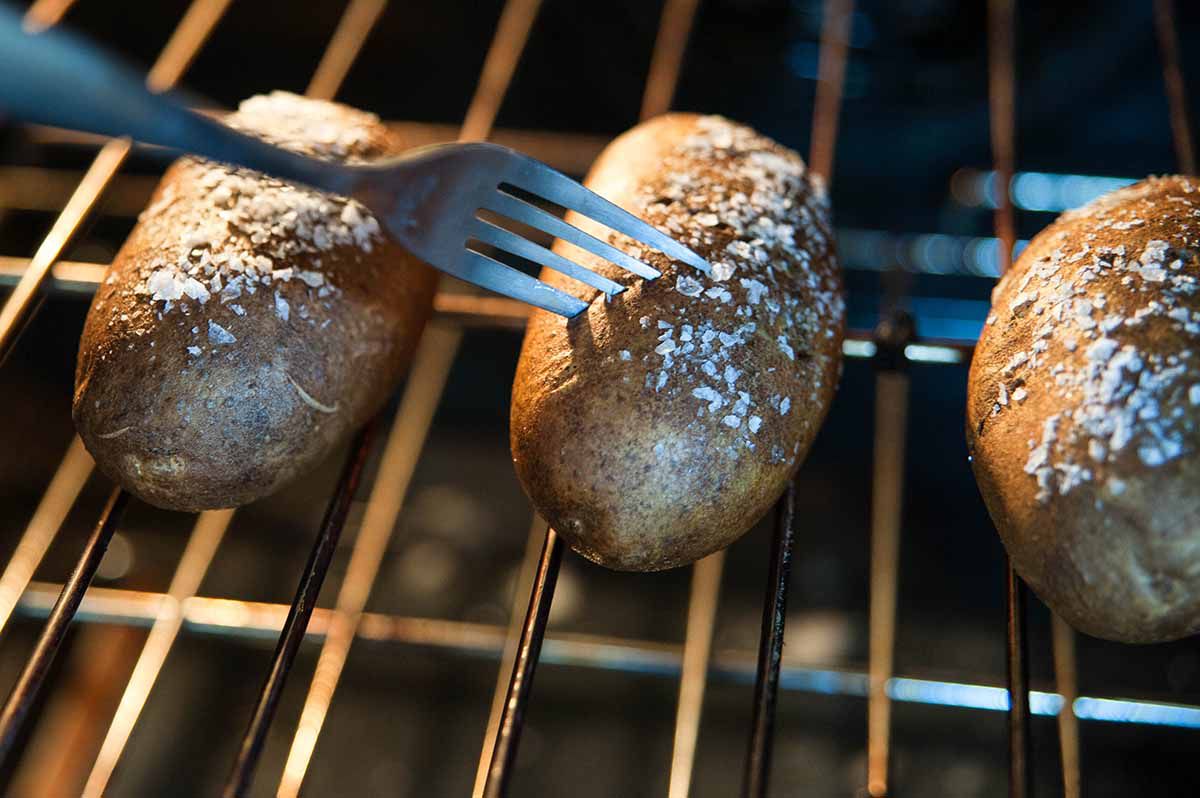 Salted potatoes on a baking in the oven with the center potato being cut into with a fork