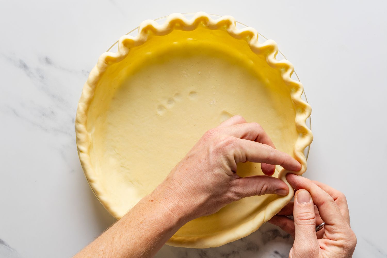 Overhead view of hands pinching the edge of a pie crust for Magic Lemon Pie recipe