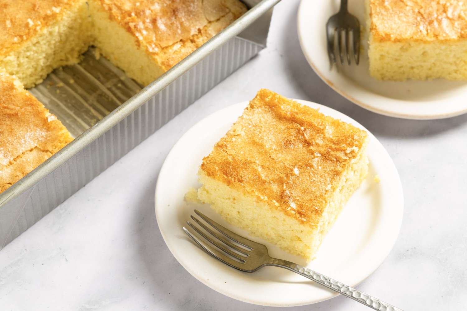 Slices of coca de llanda on plates with forks alongside a baking tray containing more slices