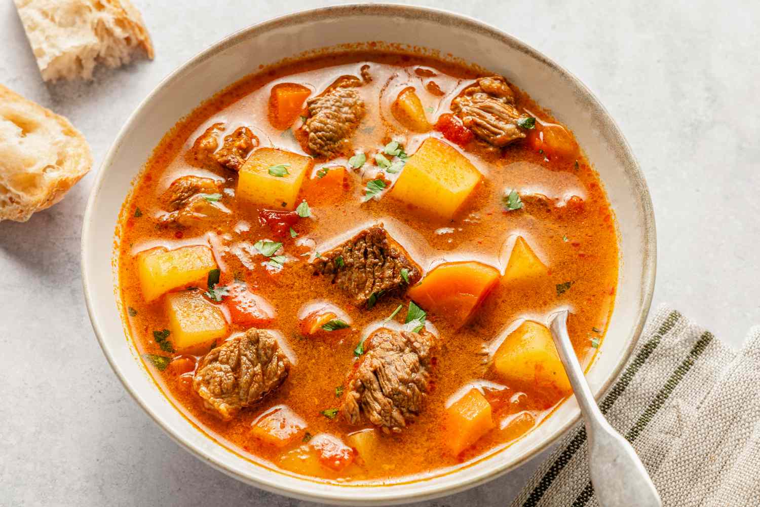 Overhead view of a bowl of Hungarian goulash with a spoon and next to some chunks of bread