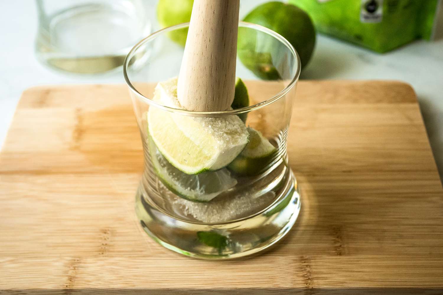Muddling limes and sugar in a rocks glass to make a lime caipirinha cocktail.