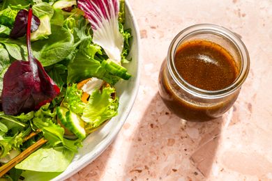 A jar of balsamic dressing next to a plate of fresh mixed salad greens