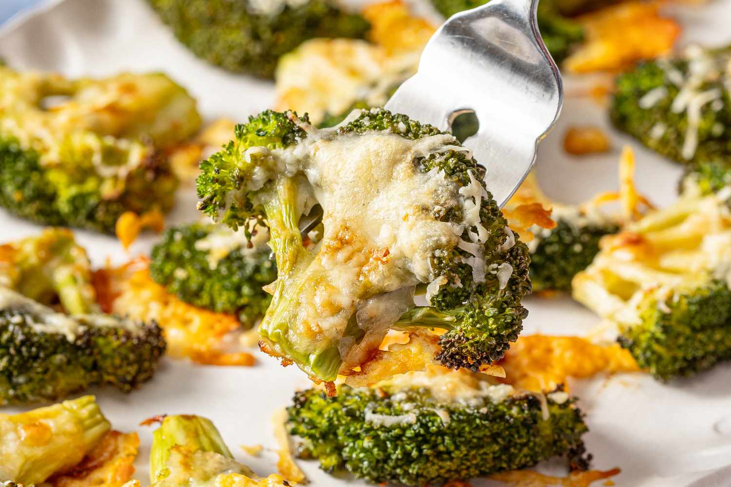 crispy parmesan broccoli lifted using a fork over a platter with more (close-up)