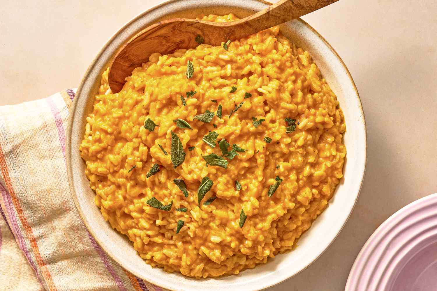 A bowl of fall risotto garnished with herbs placed with a wooden spoon