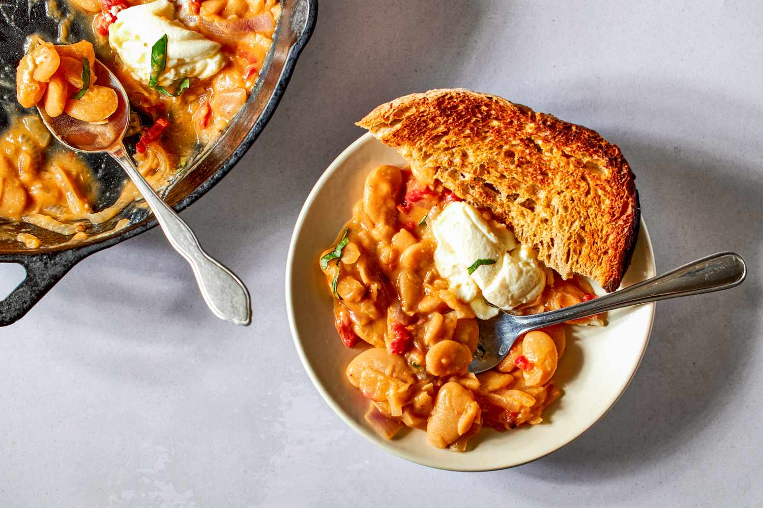 Overhead shot of a serving of Tuscan butter beans on a plate, with a dollop of ricotta on top and a slice of toasted bread on the side