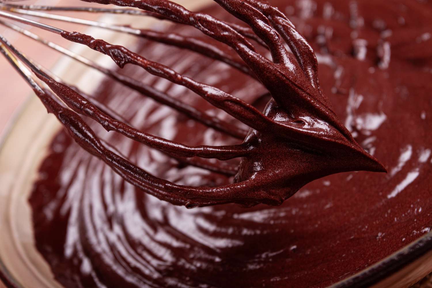 A close-up of a whisk coated in chocolate batter