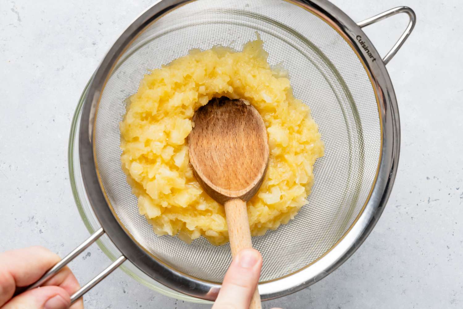 Wooden Spoon Pressing the Pineapple in the Colander to Remove Juice