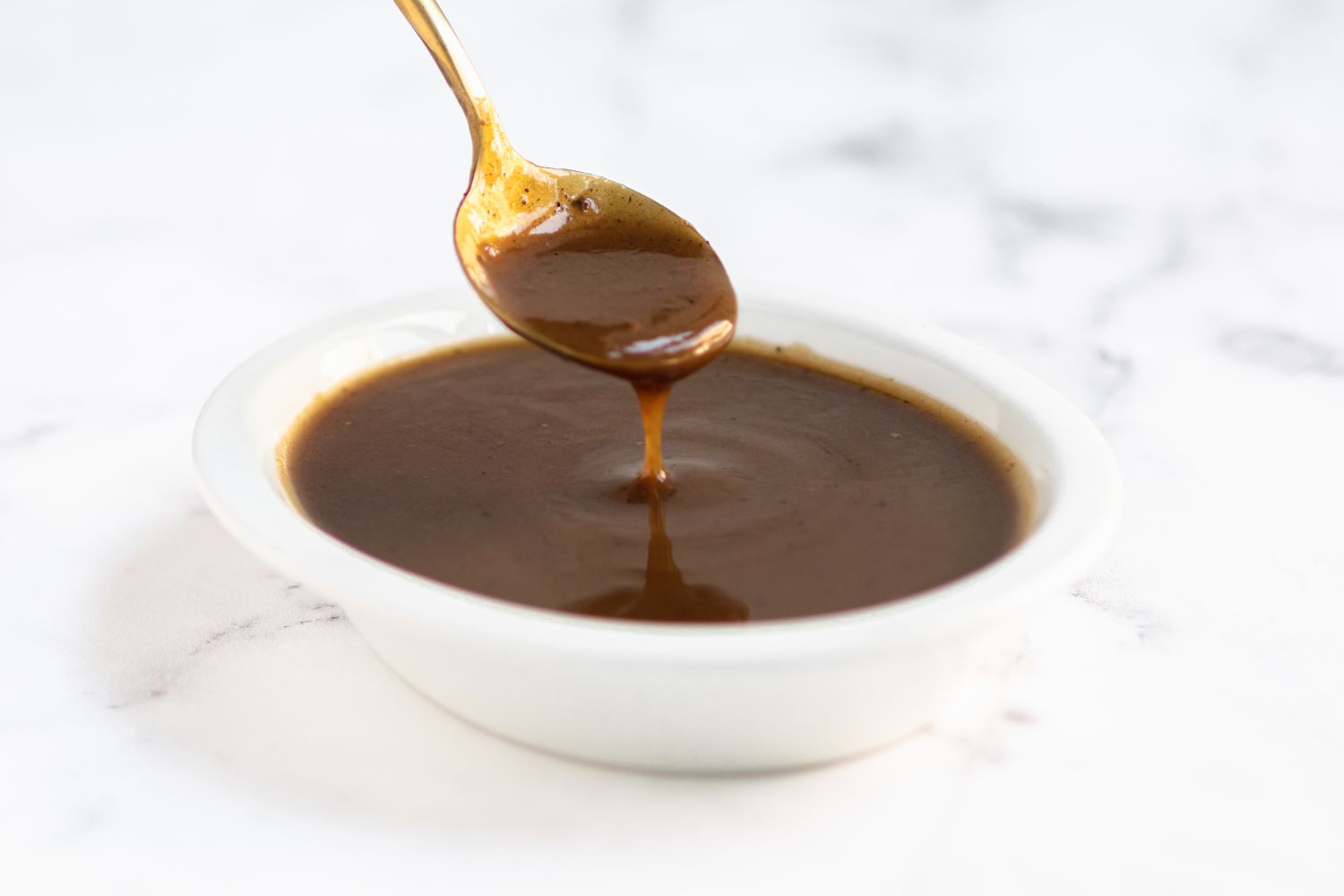 Gravy dripping off a spoon and into a white bowl
