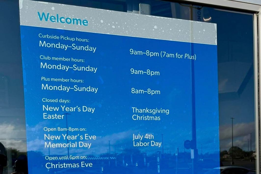 Store hours and closed days listed on a blue sign at a window display including curbside pickup member hours and holidays