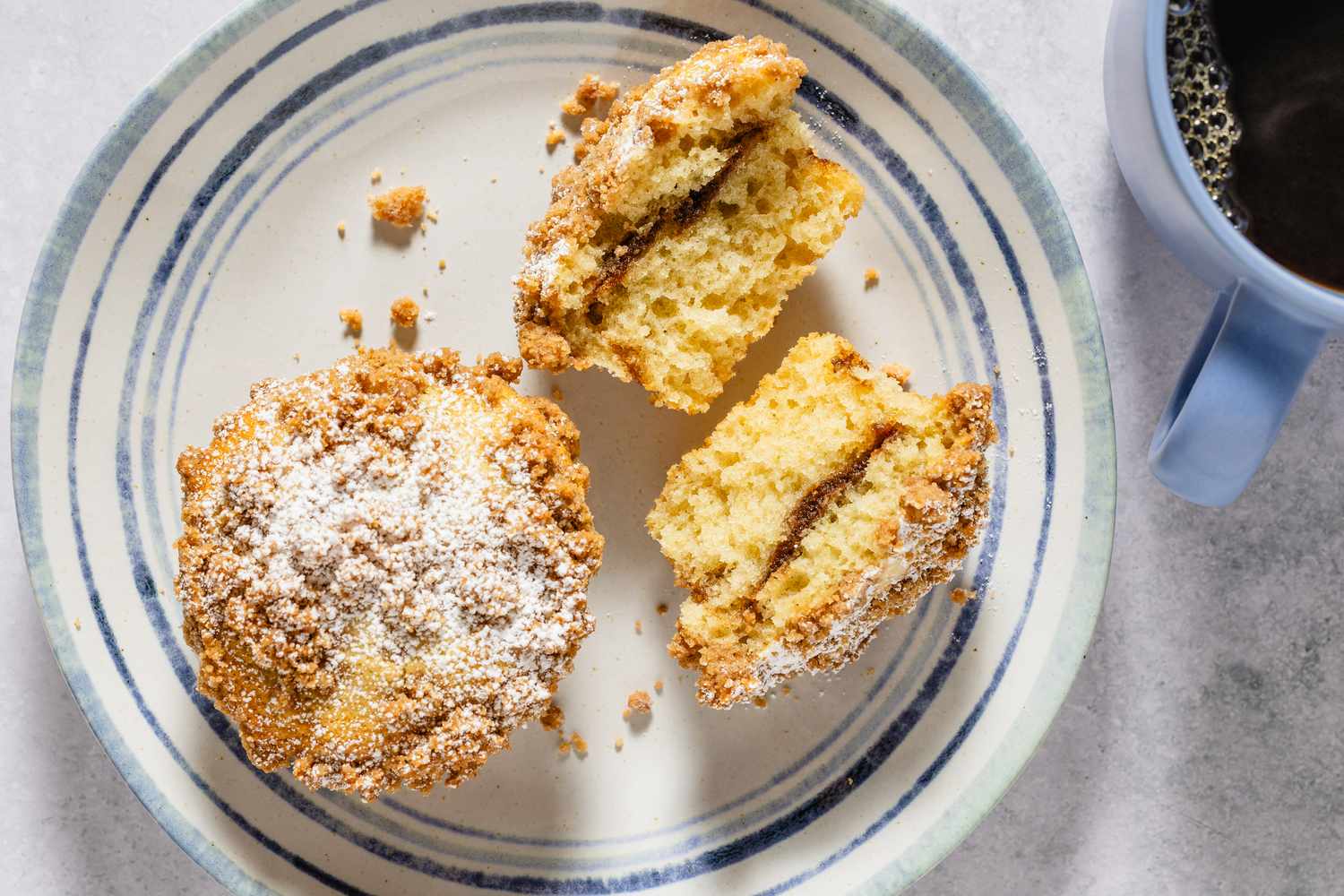 A plate with coffee cake muffins one whole and one halved next to a cup of coffee