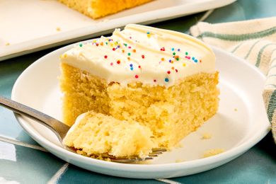 A slice of yellow cake with frosting and sprinkles on a plate with a fork holding a piece of the cake