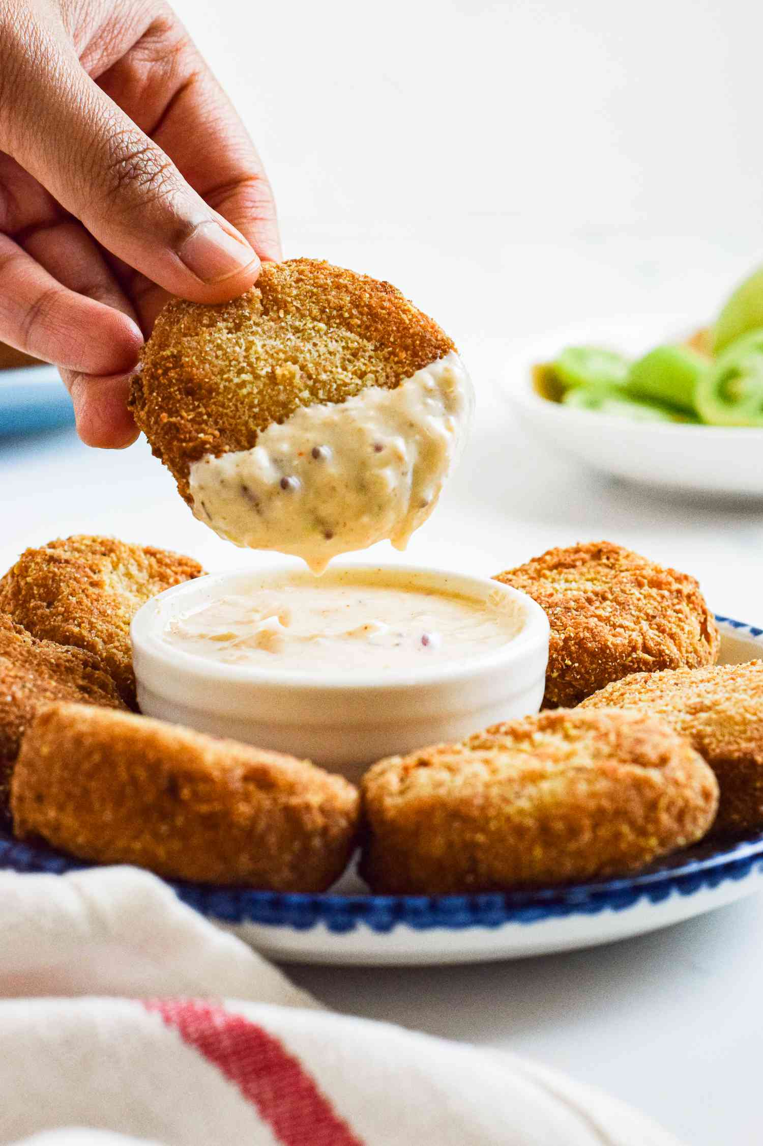 A hand lifting fried tomatoes from a bowl of dip.