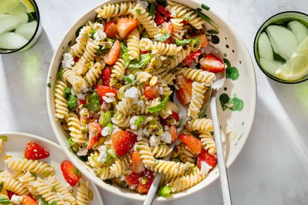 Plate of rotini pasta salad with strawberries feta and greens served on a table with glasses of water