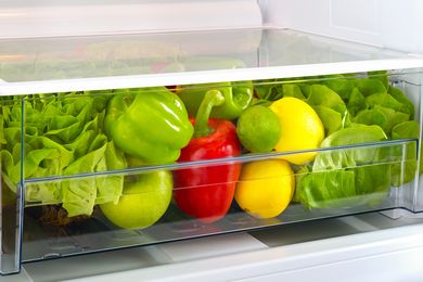 Vegetables and fruits in a refrigerator crisper drawer including lettuce bell peppers and citrus fruits
