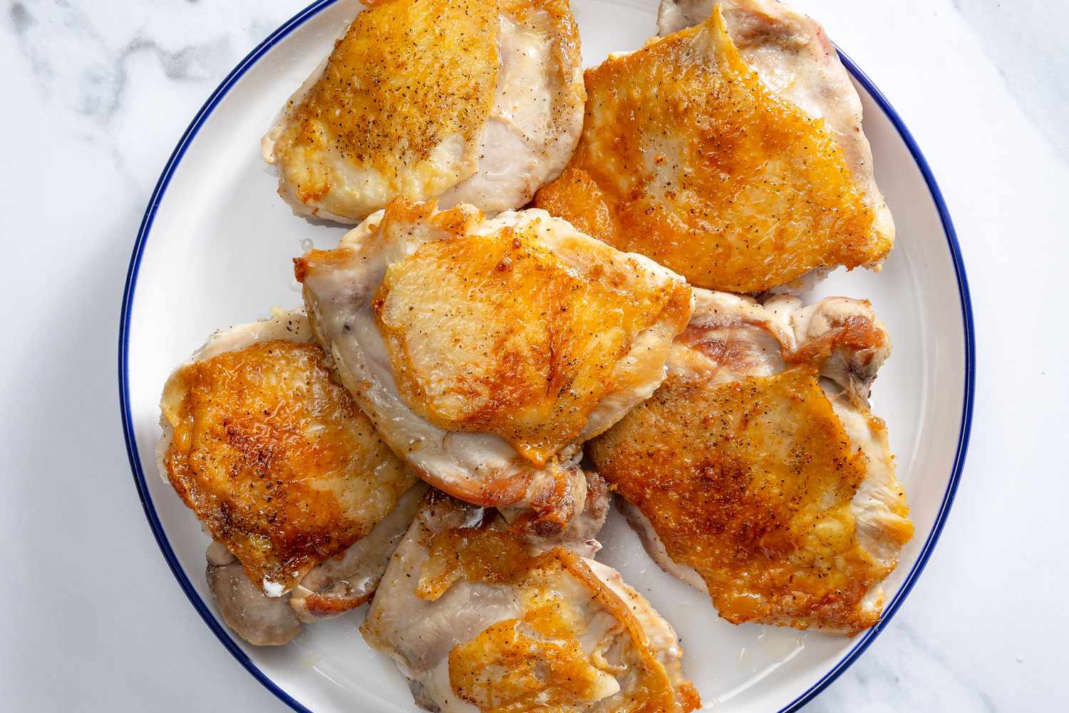 Overhead view of a white plate with blue rim with six chicken thighs after browning for Wine Chicken recipe