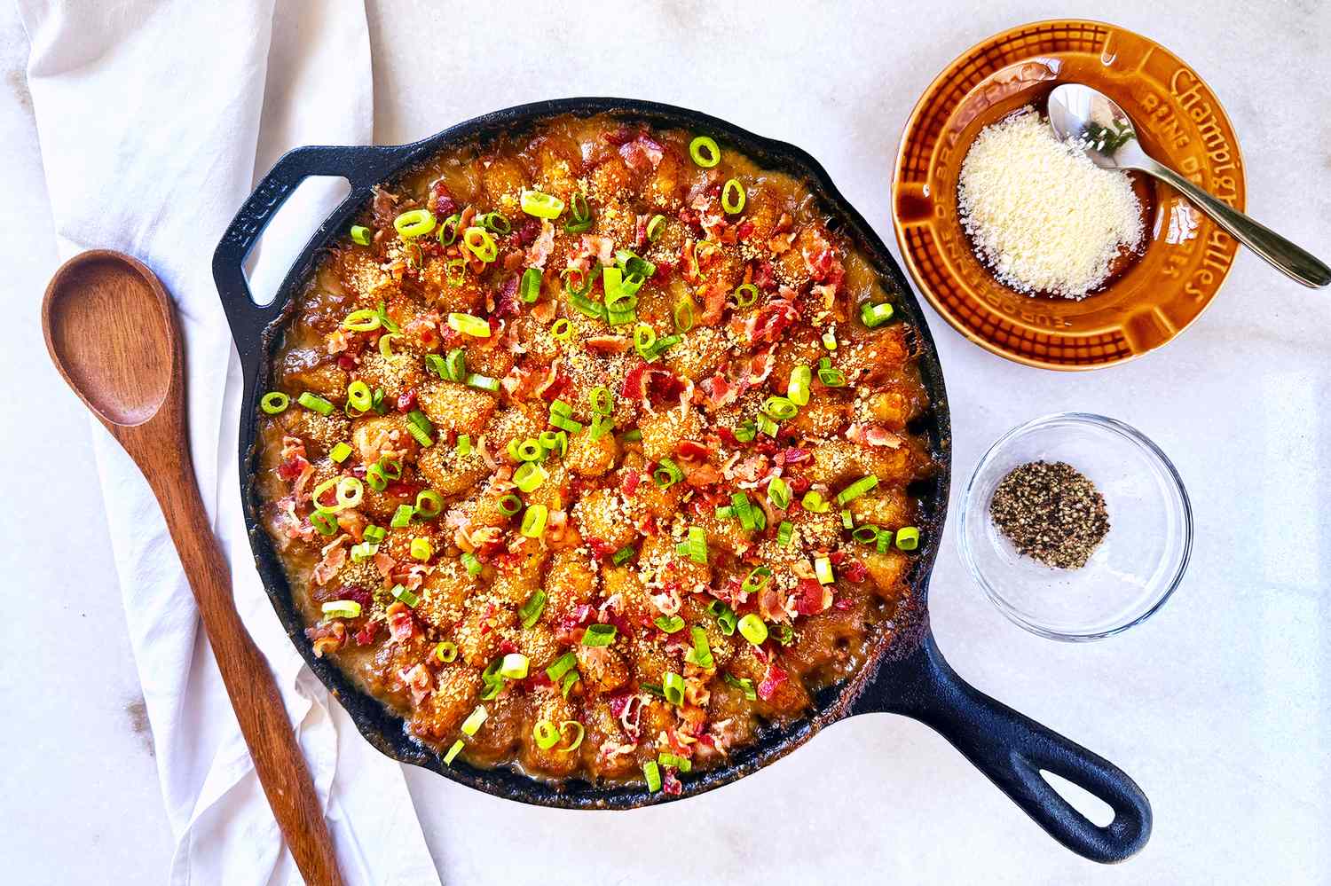 Cast iron skillet with a casserole topped with green onions served on a white background with seasoning on the side