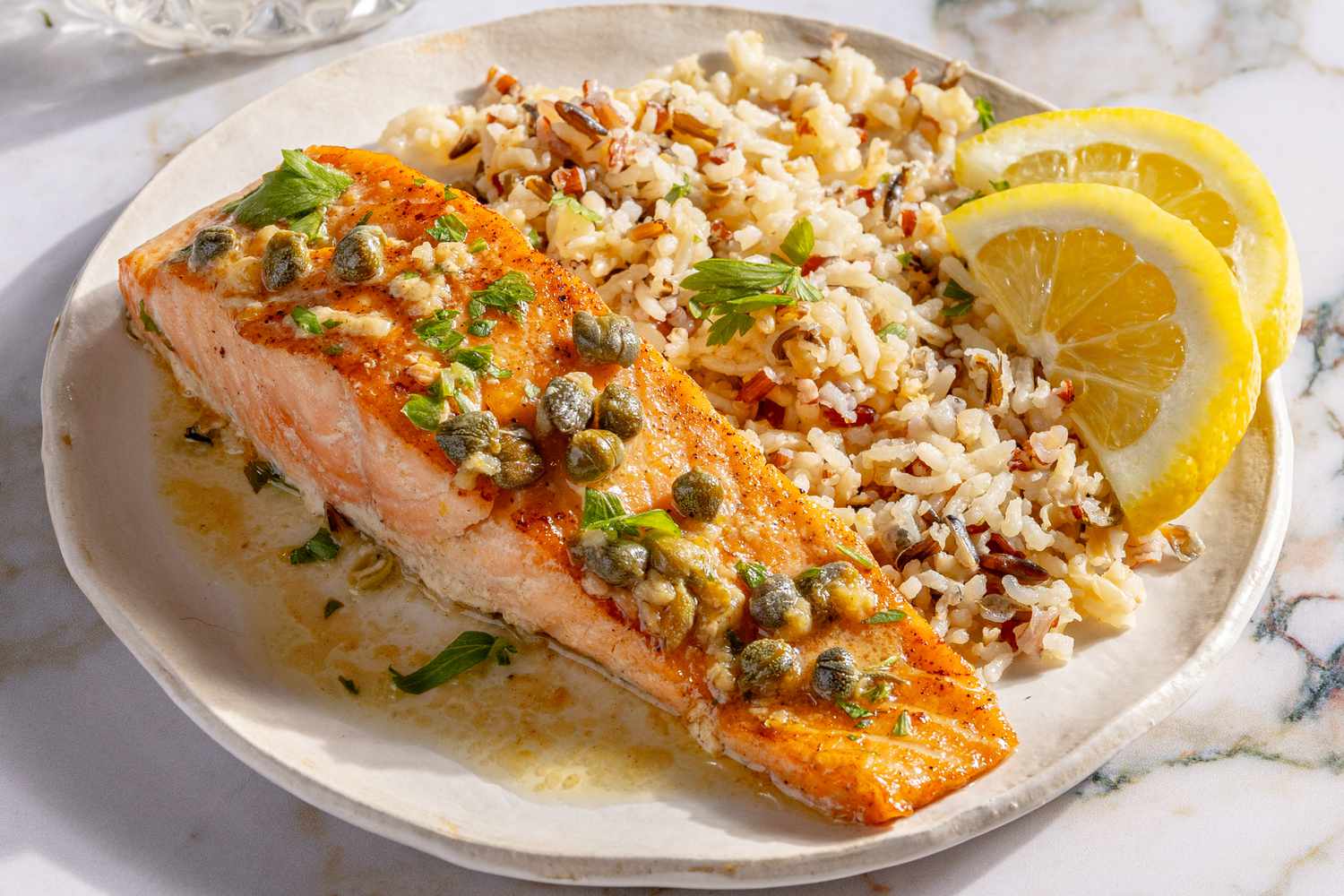 Salmon Piccata wild rice, and lemon wedges on a plate