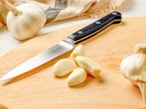 Garlic cloves and a knife on a wooden cutting board